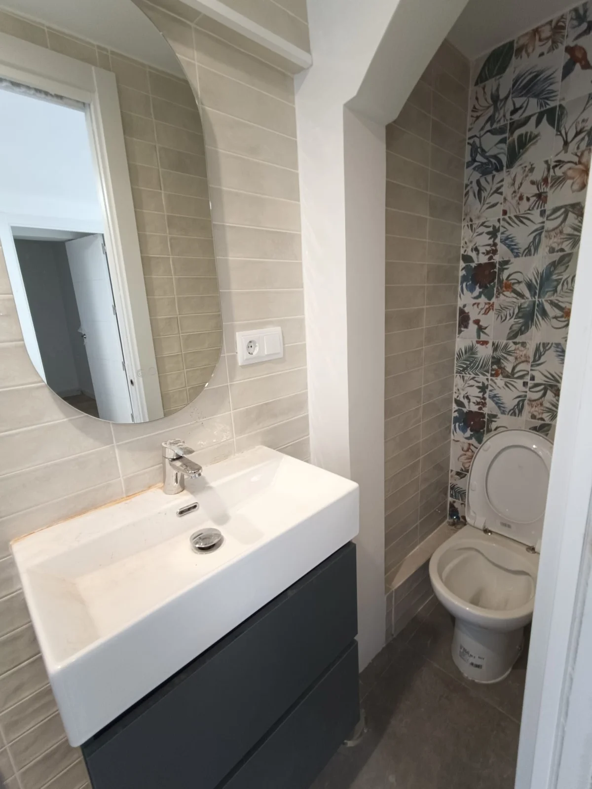 Baño con espejo ovalado, mueble suspendido y papel pintado