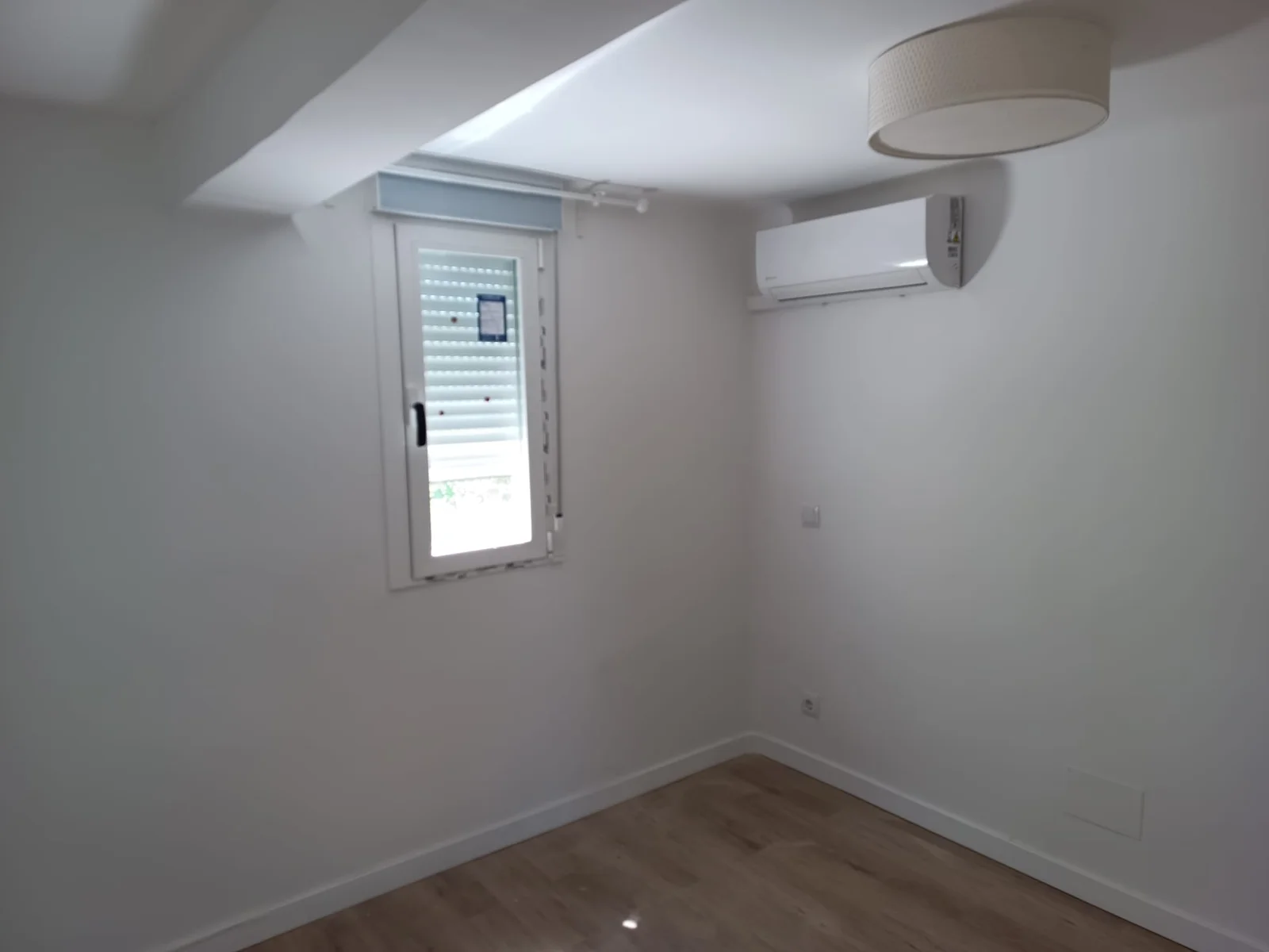 Dormitorio con ventana, split de aire y suelo de madera clara